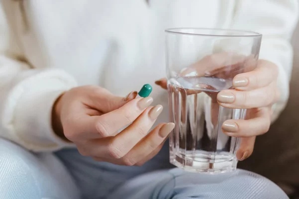 Frau hält ein Glas Wasser und eine grüne Kapsel – Symbolbild für Probiotika zur Unterstützung der Darmflora