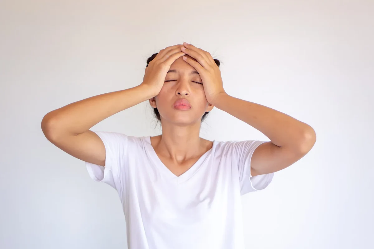 Frau hält sich mit geschlossenen Augen den Kopf vor Schmerzen