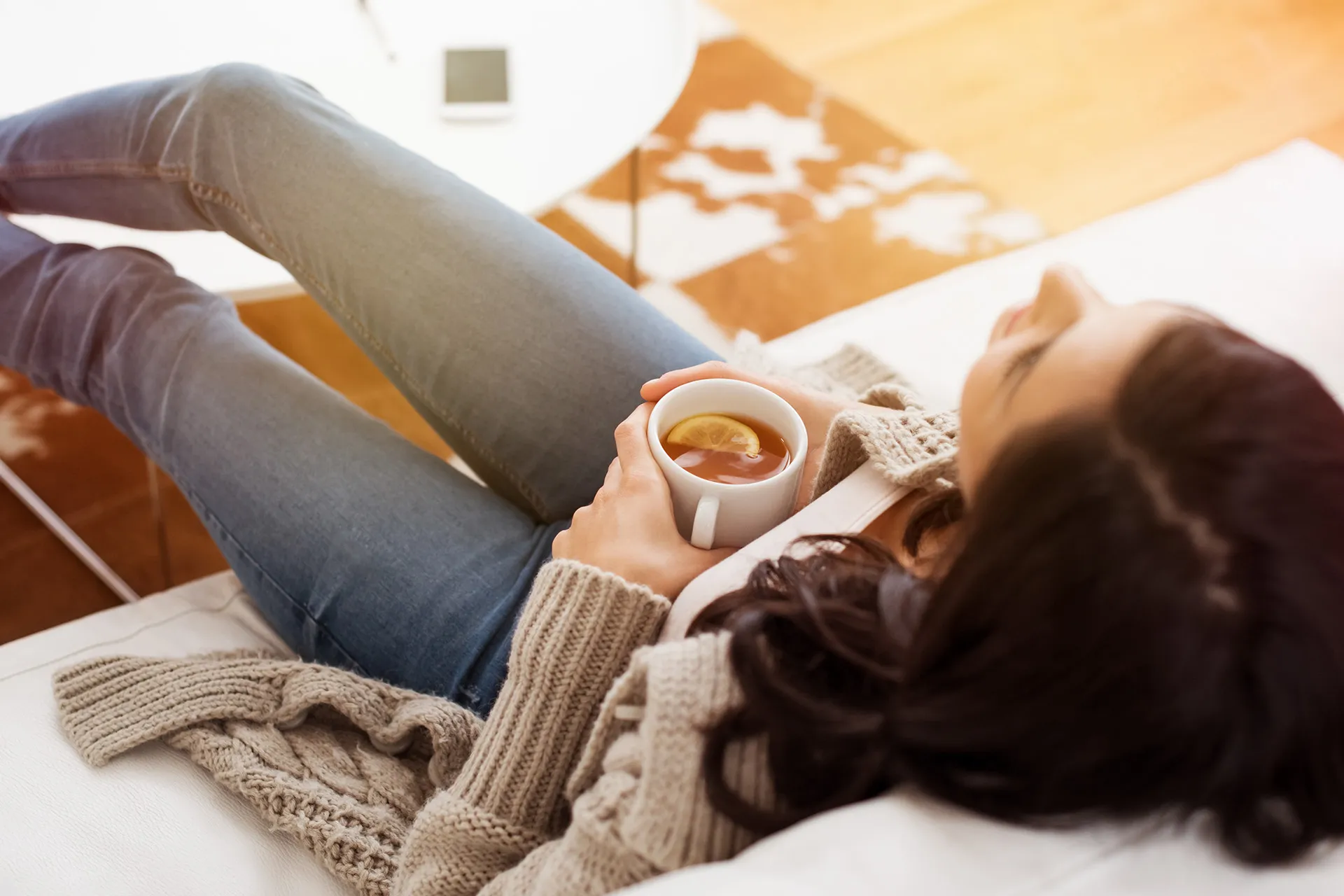Frau entspannt auf Sofa mit Tasse Tee bei Stress Magen Beschwerden
