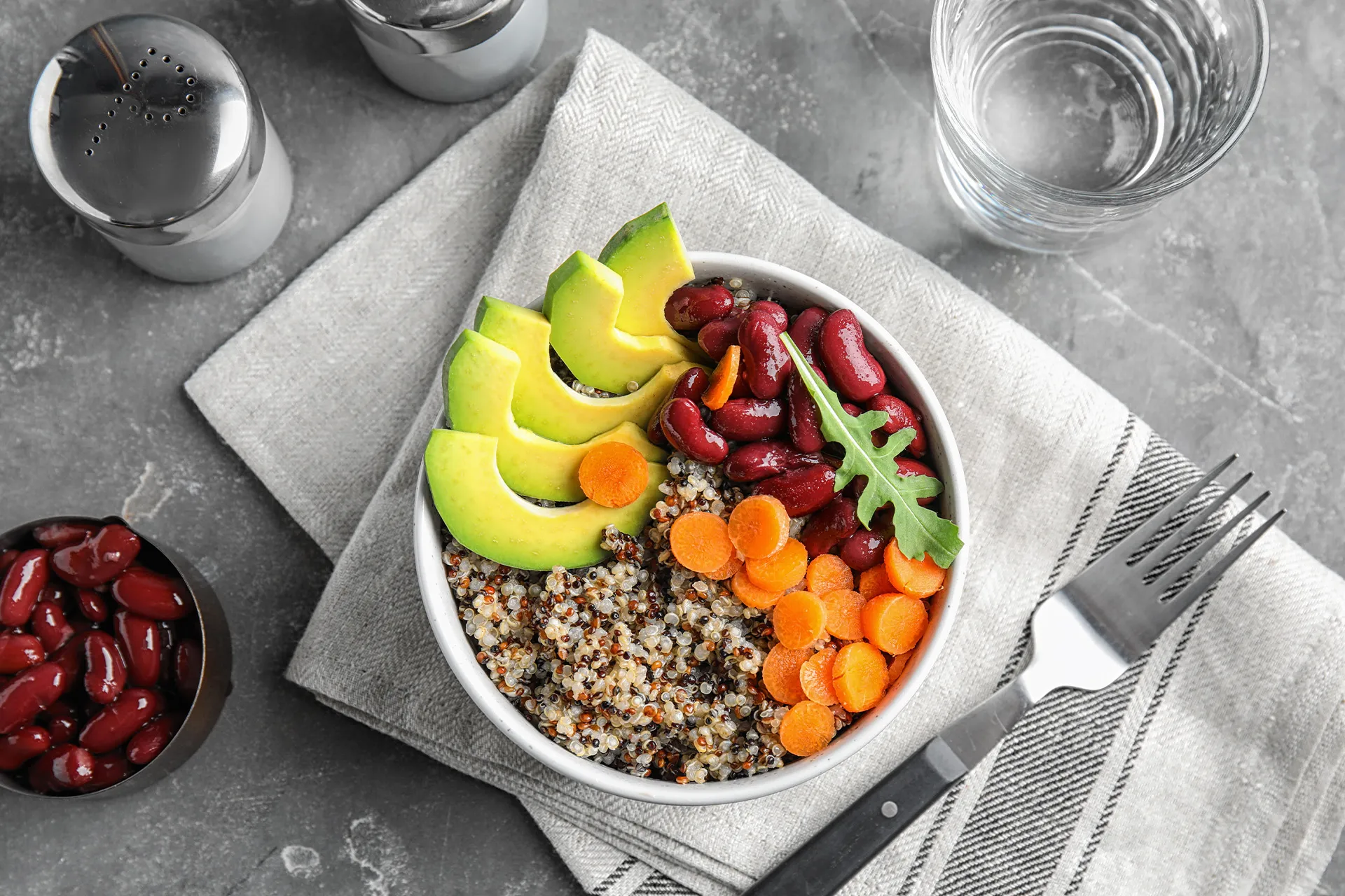 Schüssel mit Quinoa, roten Bohnen, Avocado und Karotten neben einem Glas Wasser – ballaststoffreiche Ernährung zum Verstopfung lösen